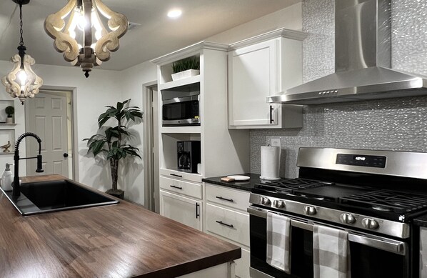 Une cuisine moderne avec des meubles blancs, une cuisinière en acier inoxydable et un plan de travail en bois.