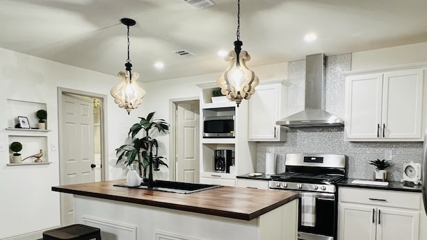 A modern kitchen with white cabinets, a central island with stools, stainless steel appliances, and pendant lighting.