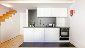 Eine kompakte Küche mit weißen Schränken, einer schwarzen Arbeitsplatte, einem Spülbecken, einer Kaffeemaschine und einem Backofen.