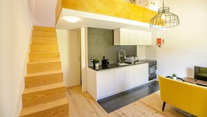A modern kitchen with a central island, a built-in oven, and a sink. There is a wooden staircase leading to an upper level.