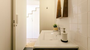 A modern bathroom with a white sink, a mirror, and a small plant on the countertop.