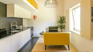 A modern kitchen with a black countertop, stainless steel appliances, and a yellow chair in the living area.