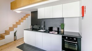 Cozinha moderna com armários brancos, bancada preta, forno embutido e escada de madeira.