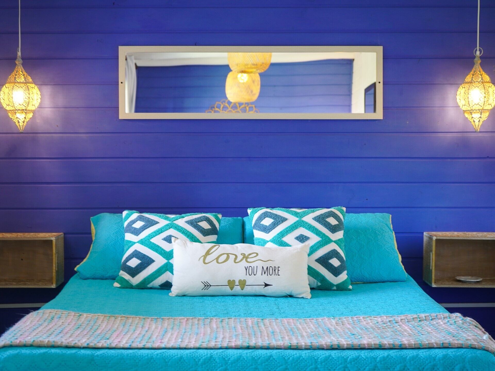 A bed with teal bedding, two patterned pillows, and a decorative pillow with text.