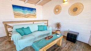 A cozy room with a wooden bench, a light blue sofa, and a painting of a beach scene. - Cabañas Kundalini Punta de Diablo (Punta del Diablo)