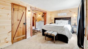 Un dormitorio de cabaña de madera con cama, banca y puerta que da a una zona de cocina.