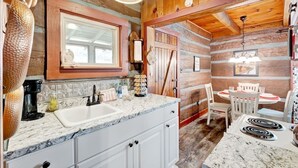 Una cocina rústica con paredes de madera, encimera de mármol y zona de comedor con sillas blancas.