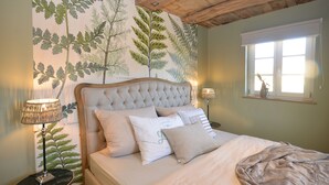 Ein Schlafzimmer mit einer geblümten Kopfstütze, einem großen Fenster mit Blick und einer Wand mit botanischem Wandpapier.