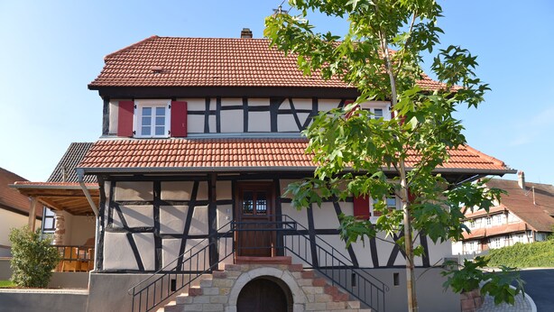 Ein traditionelles Fachwerkhäuschen mit rotem Ziegeldach, einer Holztür und einer Steintreppe, die zum Eingang führt.