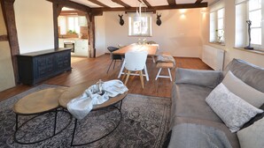 Ein großzügiger Wohnbereich mit Holzboden, einem grauen Sofa, einem runden Couchtisch und einem Esstisch mit Stühlen.
