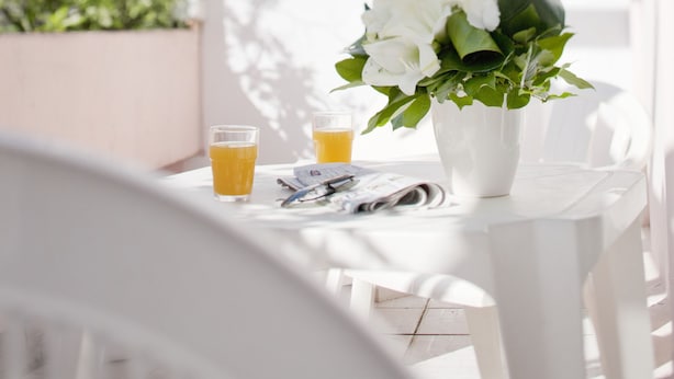 A white outdoor seating area with a table, chairs, a potted plant, and a glass of orange juice. - hotel thermes les Ecureuils (Dax)