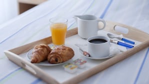 A breakfast tray with croissants, orange juice, coffee, and a spoon on a bed with a striped bedspread and a wooden headboard. - hotel thermes les Ecureuils (Dax)