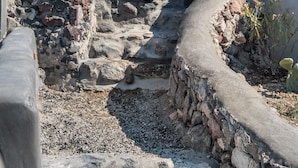 A coastal building with a stone pathway leading to a white structure. - Three Caves - Villa With Private Pool Sea View (Santorini)