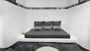 A bed with a black mattress and pillows, a white wall, and a stone ledge. - Three Caves - Villa With Private Pool Sea View (Santorini)