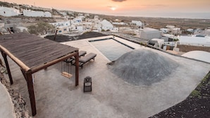 A rooftop terrace with a wooden table, lounge chairs, and a small pool. - Three Caves - Villa With Private Pool Sea View (Santorini)