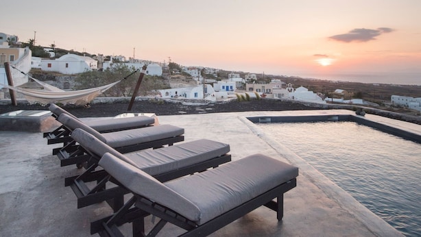 A rooftop pool area with lounge chairs and a view of a coastal village at sunset. - Three Caves - Villa With Private Pool Sea View (Santorini)