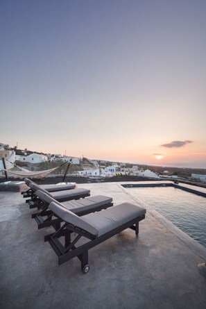 Un espace piscine aménagé sur le toit, avec des chaises longues et une vue sur un village côtier au coucher du soleil.