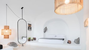 A modern bedroom with a large bed, a round black rug, and a hanging light fixture. - Three Caves - Villa With Private Pool Sea View (Santorini)