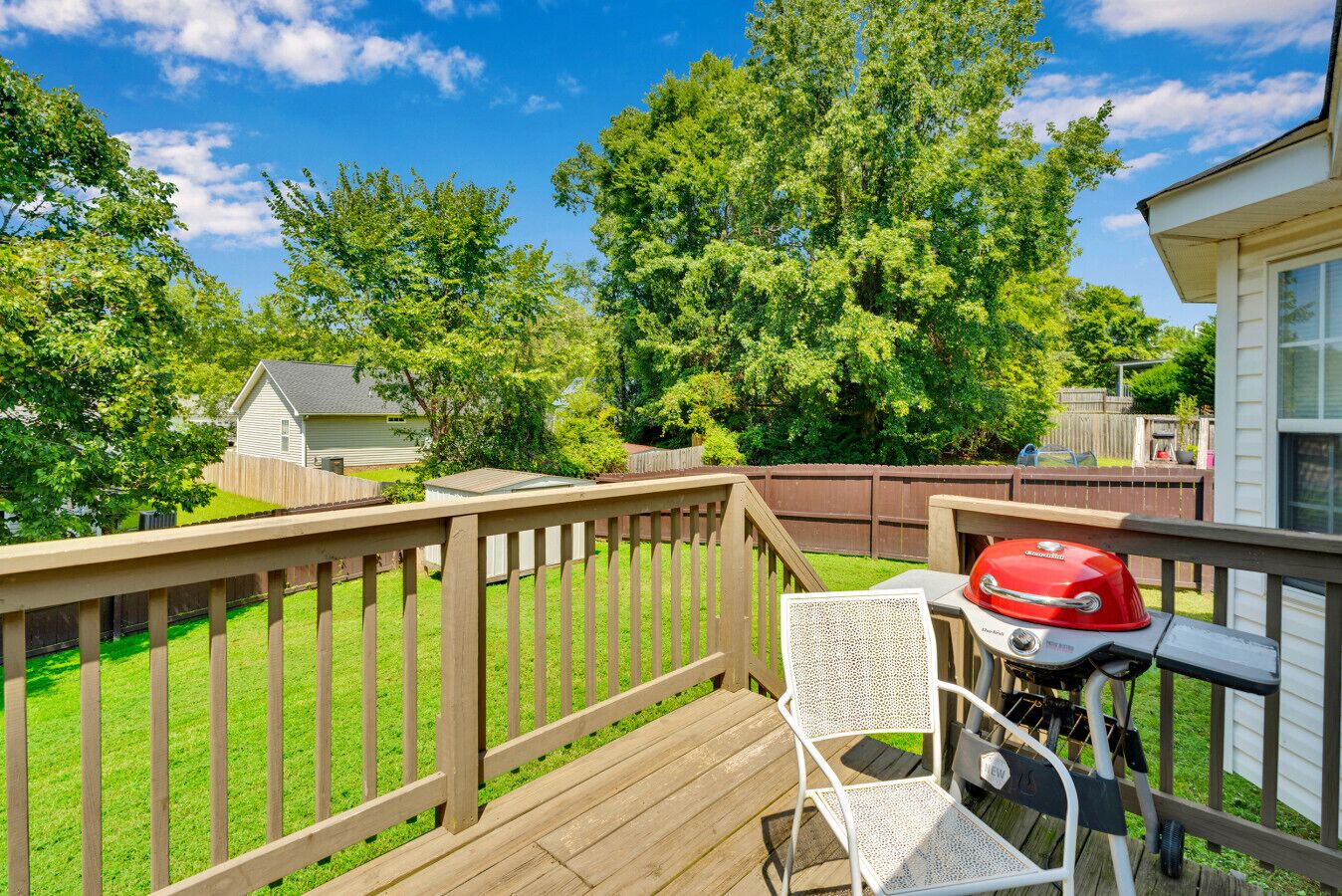 A deck with a grill and a chair, surrounded by a wooden fence and trees.