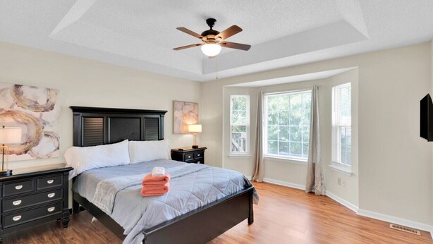 Une chambre à coucher avec un lit, des tables de chevet, un ventilateur de plafond et une grande fenêtre.