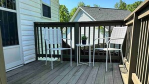 Une terrasse en bois avec un paillasson, deux chaises blanches et une petite table.