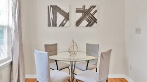 Un coin repas comprenant une table ronde en verre, quatre chaises et deux tableaux abstraits accrochés au mur.