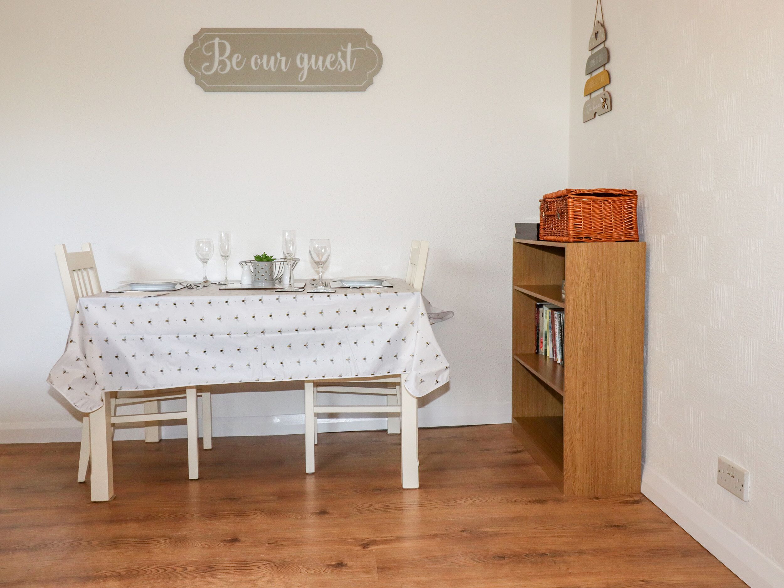 A dining area with a table set for four, a bookshelf, and a sign on the wall.