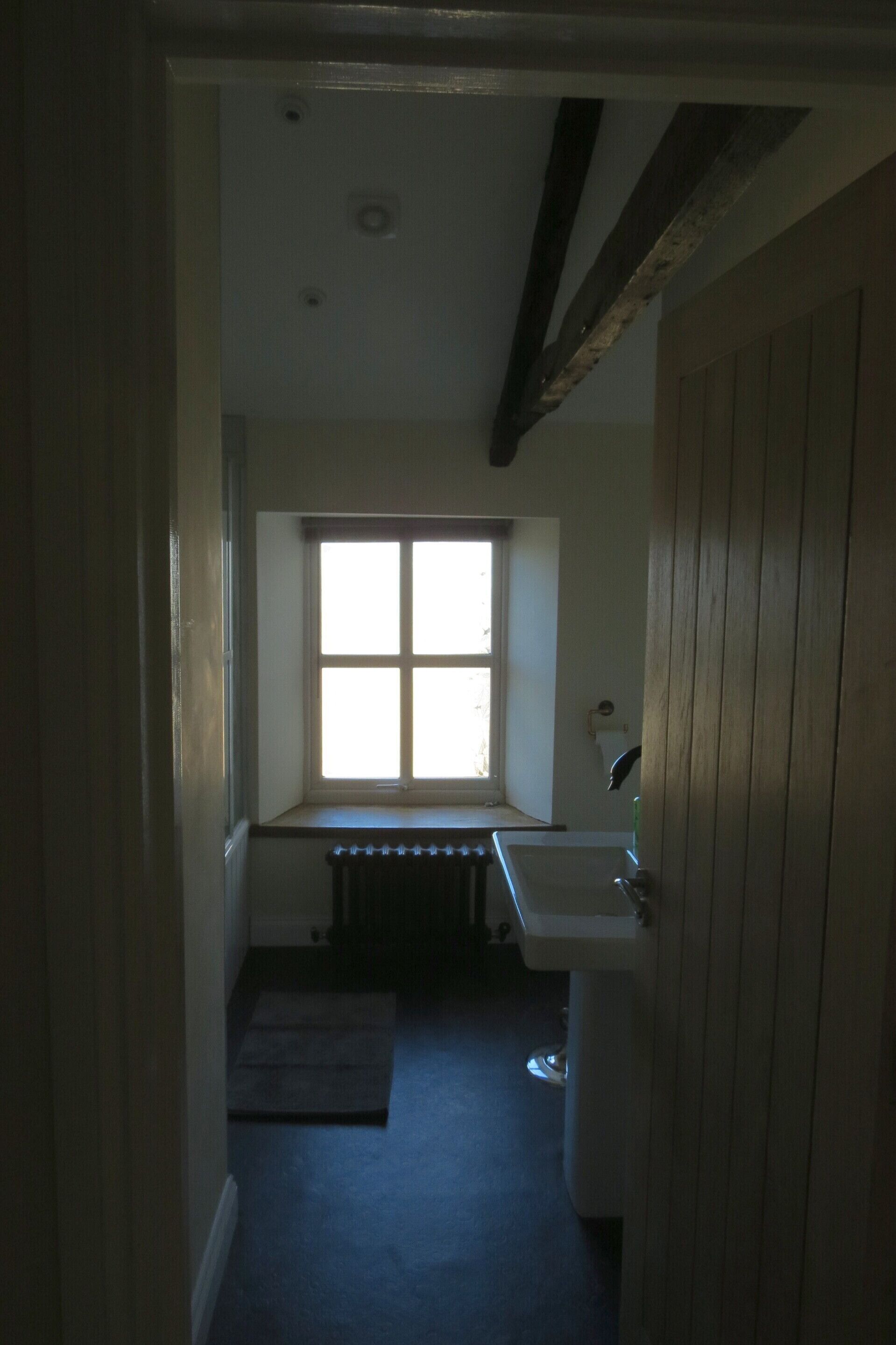 Ein schmaler Flur, der zu einem kleinen Badezimmer mit Fenster, Heizkörper und Waschbecken führt.