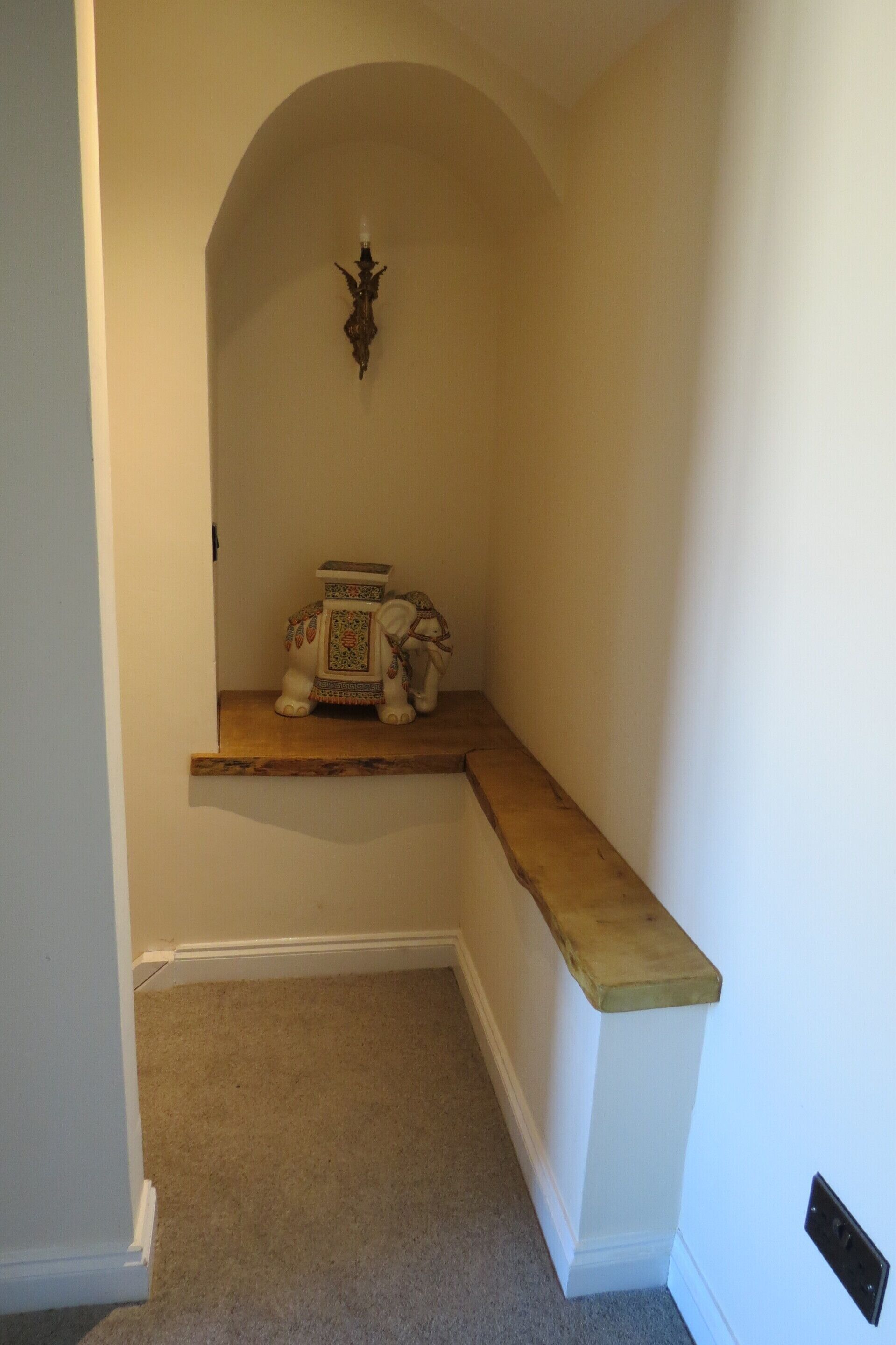 A narrow hallway with a wooden shelf, a decorative wall sconce, and a carpeted floor.