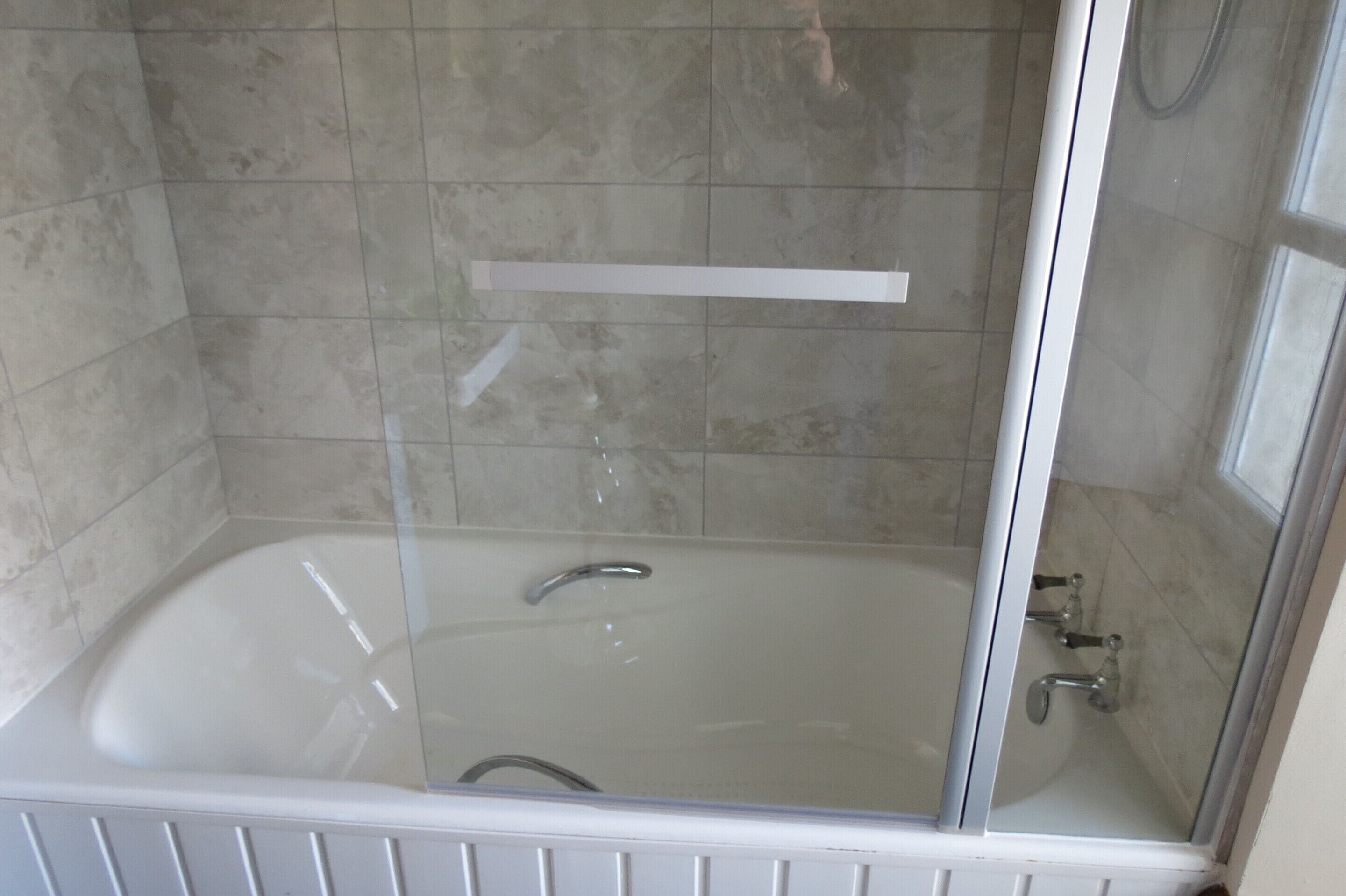 A glass-enclosed bathtub with a showerhead and a control panel.