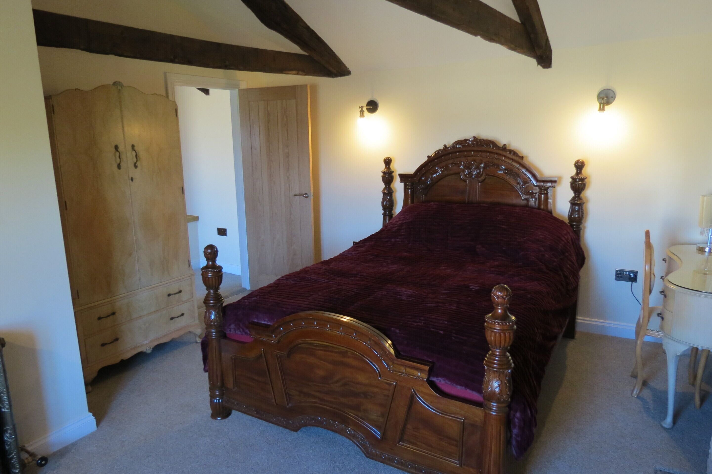 A bedroom with a wooden four-poster bed, a wooden wardrobe, and a bedside table with a lamp.