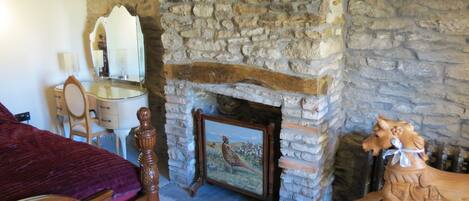 A bedroom with a stone fireplace, a bed with a red blanket, a wooden dresser, and a wooden horse sculpture.