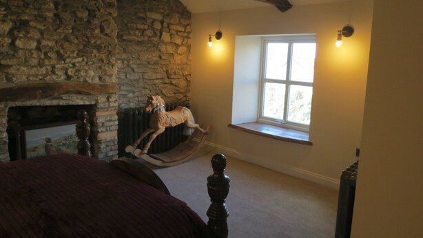 A bedroom with a stone wall, a wooden rocking horse, a fireplace, and a window with a view. - Farthing Cottage (Bishop Auckland)
