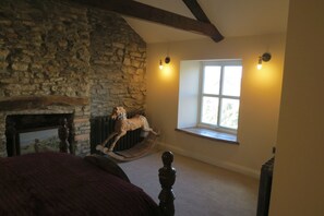 A bedroom with a stone wall, a wooden rocking horse, a fireplace, and a window with a view. - Farthing Cottage (Bishop Auckland)