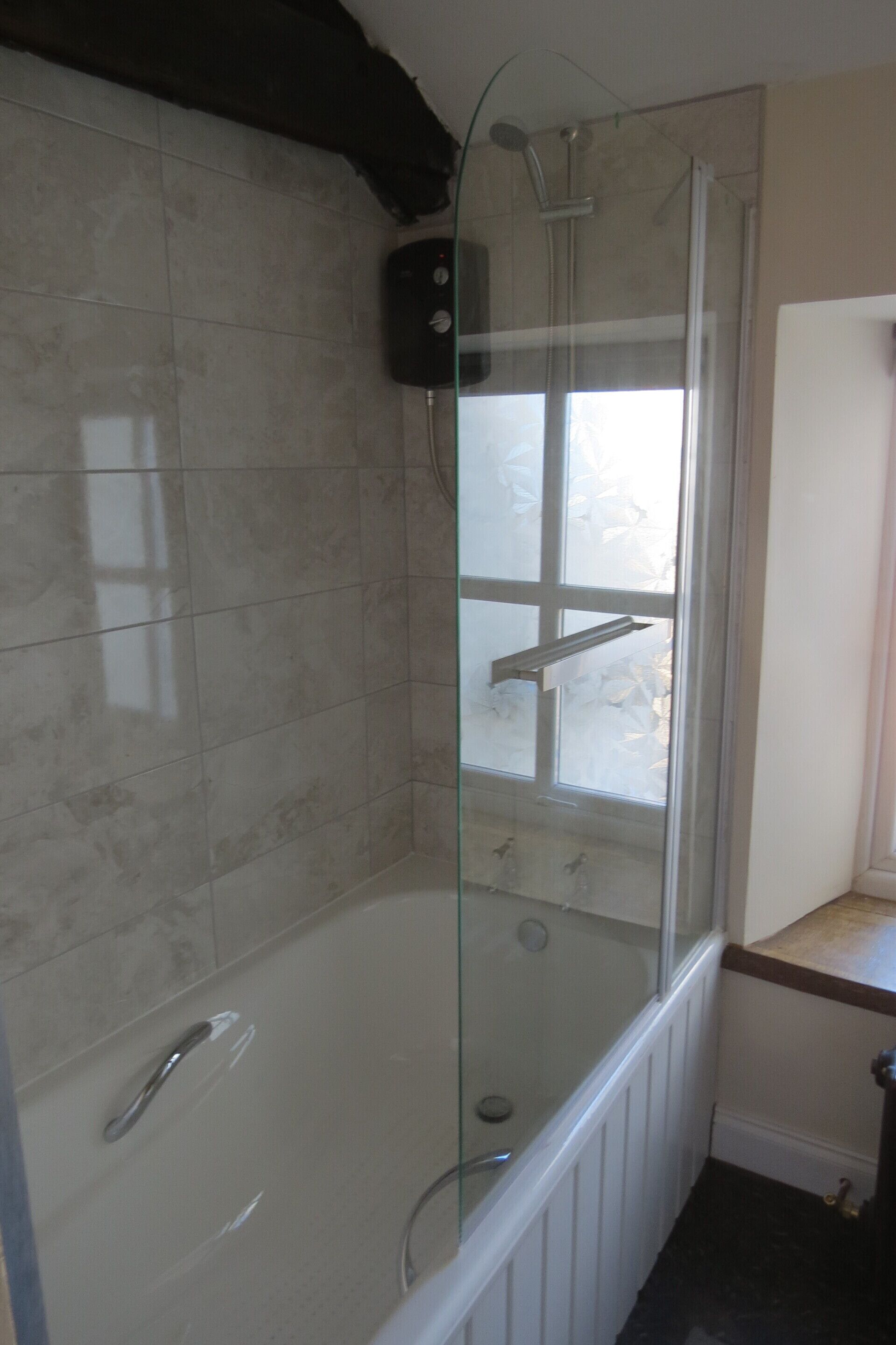 A glass-enclosed shower with a white tub, tiled walls, and a visible window.