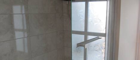 A glass-enclosed shower with a white tub, tiled walls, and a visible window.