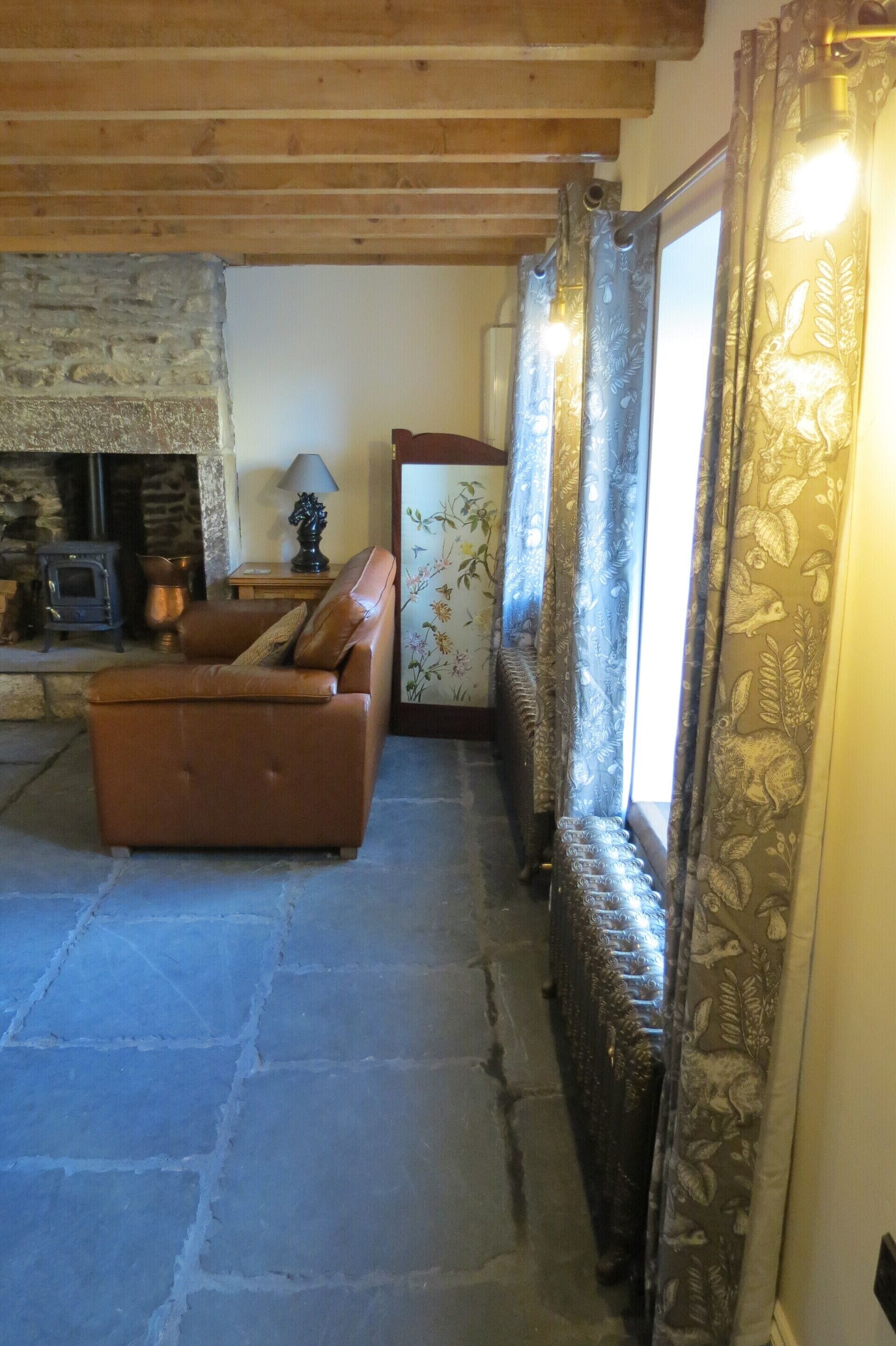 A cozy living room with a stone fireplace, a leather sofa, and patterned curtains.