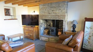 A cozy living room with leather sofas, a stone fireplace, a television, and wooden furniture. - Farthing Cottage (Bishop Auckland)
