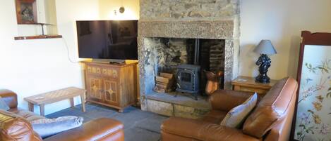 A cozy living room with leather sofas, a stone fireplace, a television, and wooden furniture.