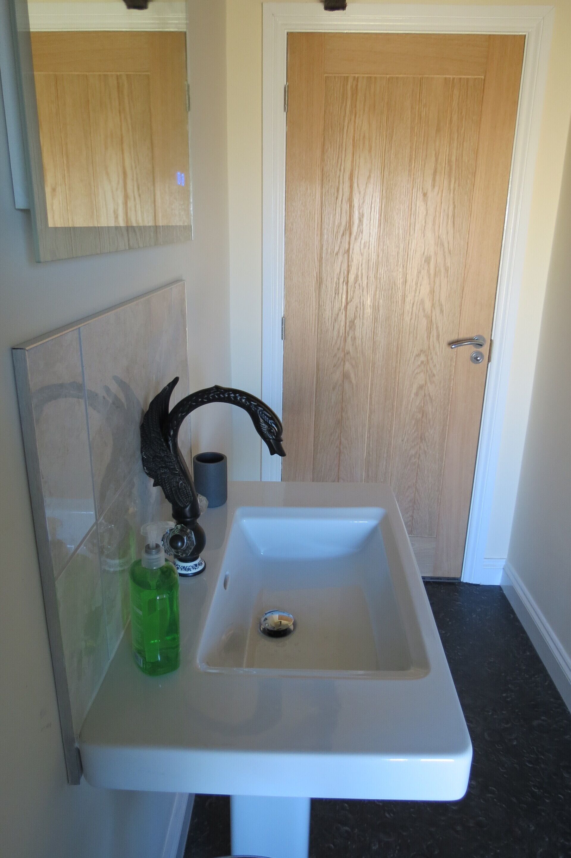 Ein Badezimmer mit einem weißen Waschbecken, einem dekorativen Wasserhahn, einer grünen Flasche und einer Holztür im Hintergrund.
