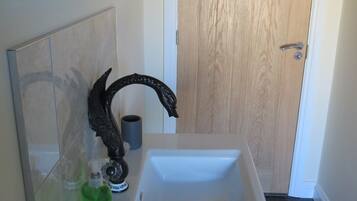 Ein Badezimmer mit einem weißen Waschbecken, einem dekorativen Wasserhahn, einer grünen Flasche und einer Holztür im Hintergrund.
