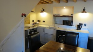 A compact kitchen with a wooden table, a washing machine, and a microwave. - Farthing Cottage (Bishop Auckland)