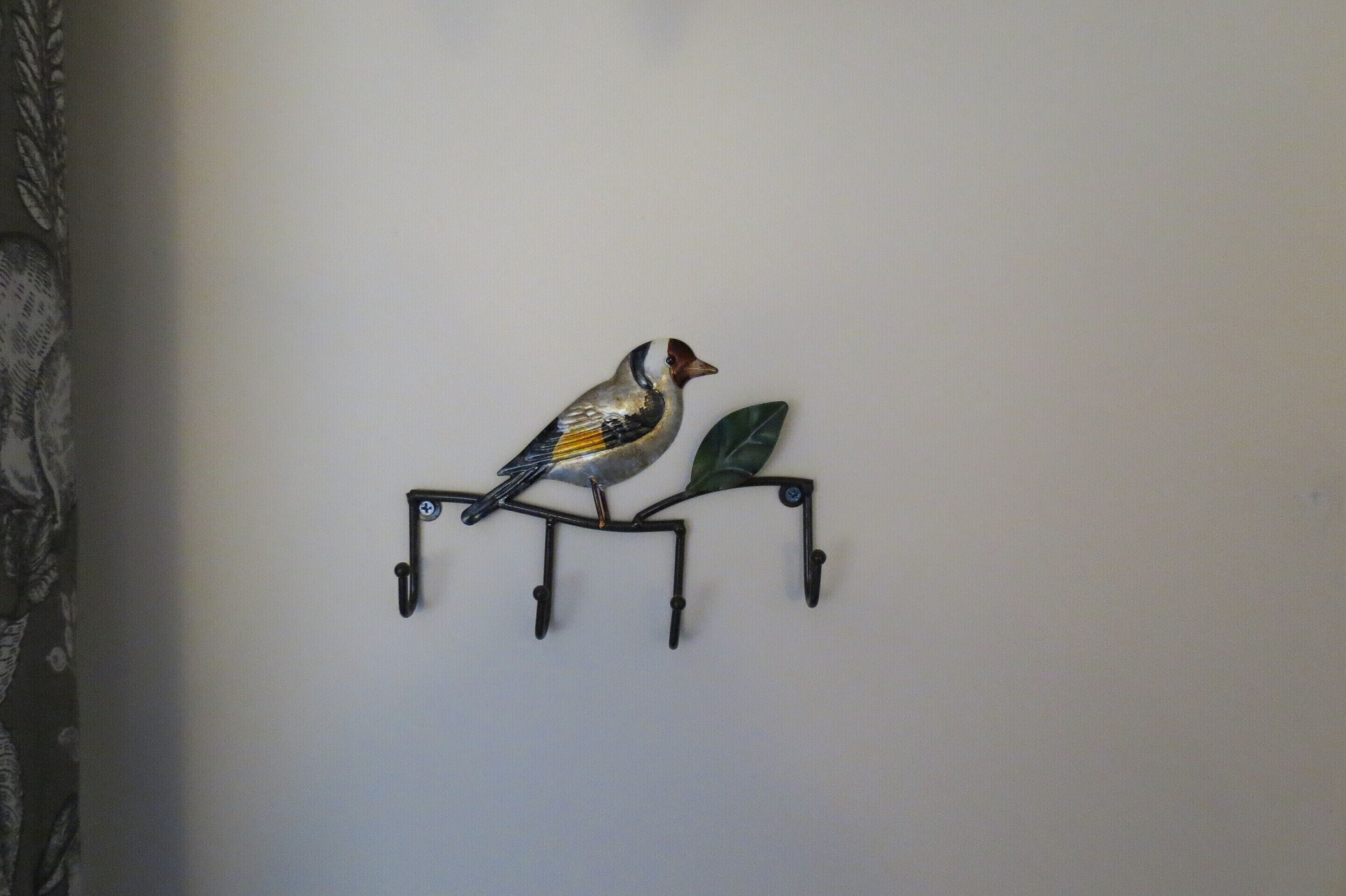 A wall-mounted metal bird sculpture with a branch and a leaf.