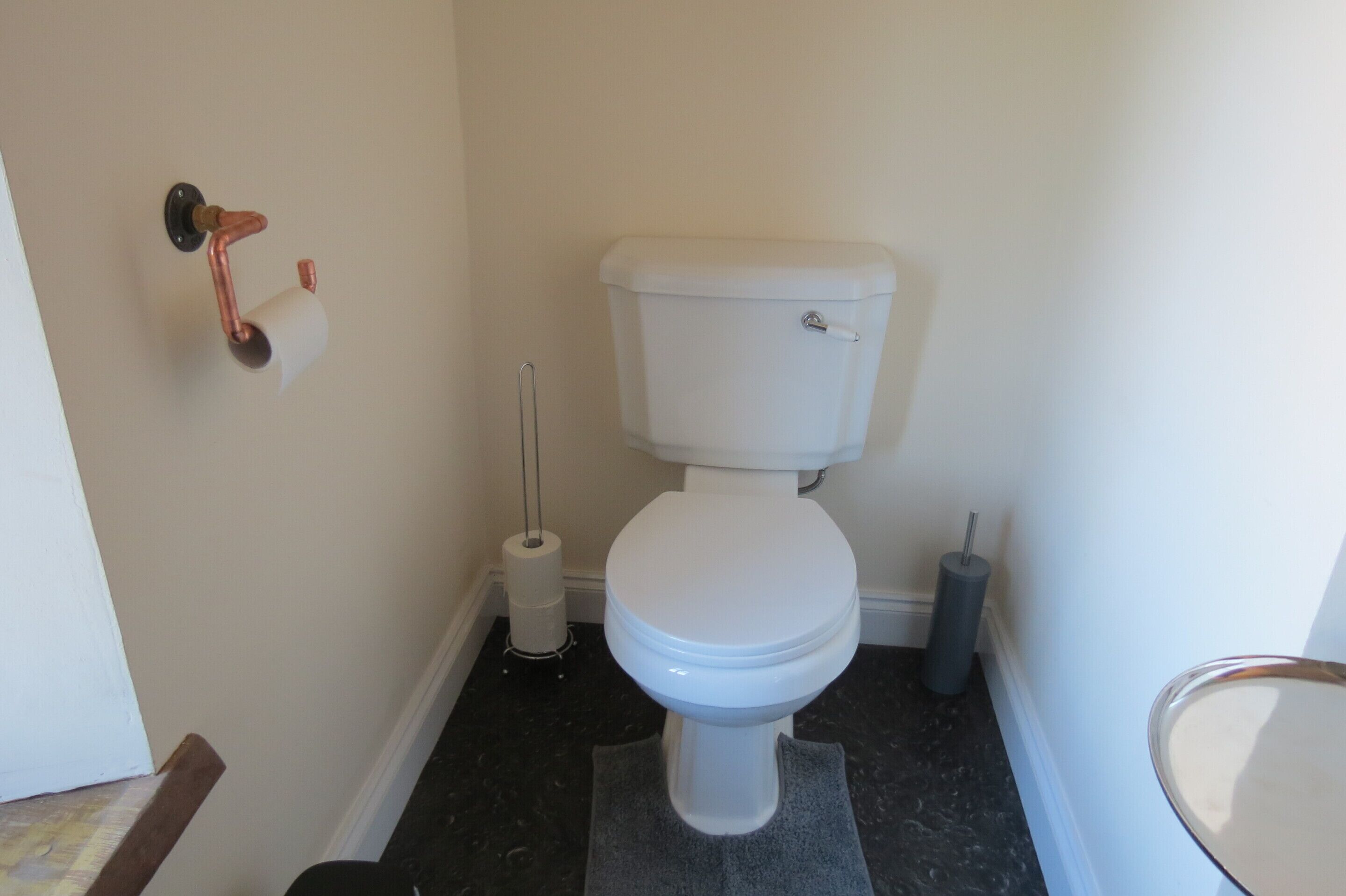 Et badeværelse med et hvidt toilet, toiletpapir og en toiletbørste.