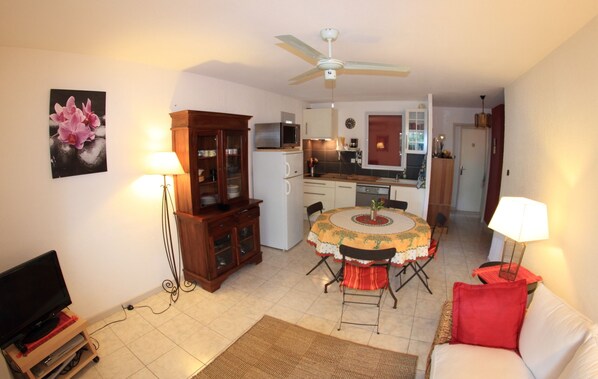 A compact living space with a dining area, kitchenette, and a television in the corner.