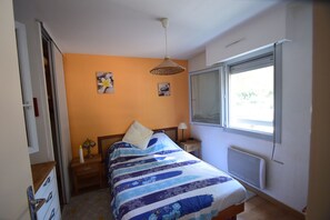 A bedroom with a bed, a nightstand, a window, and a radiator.