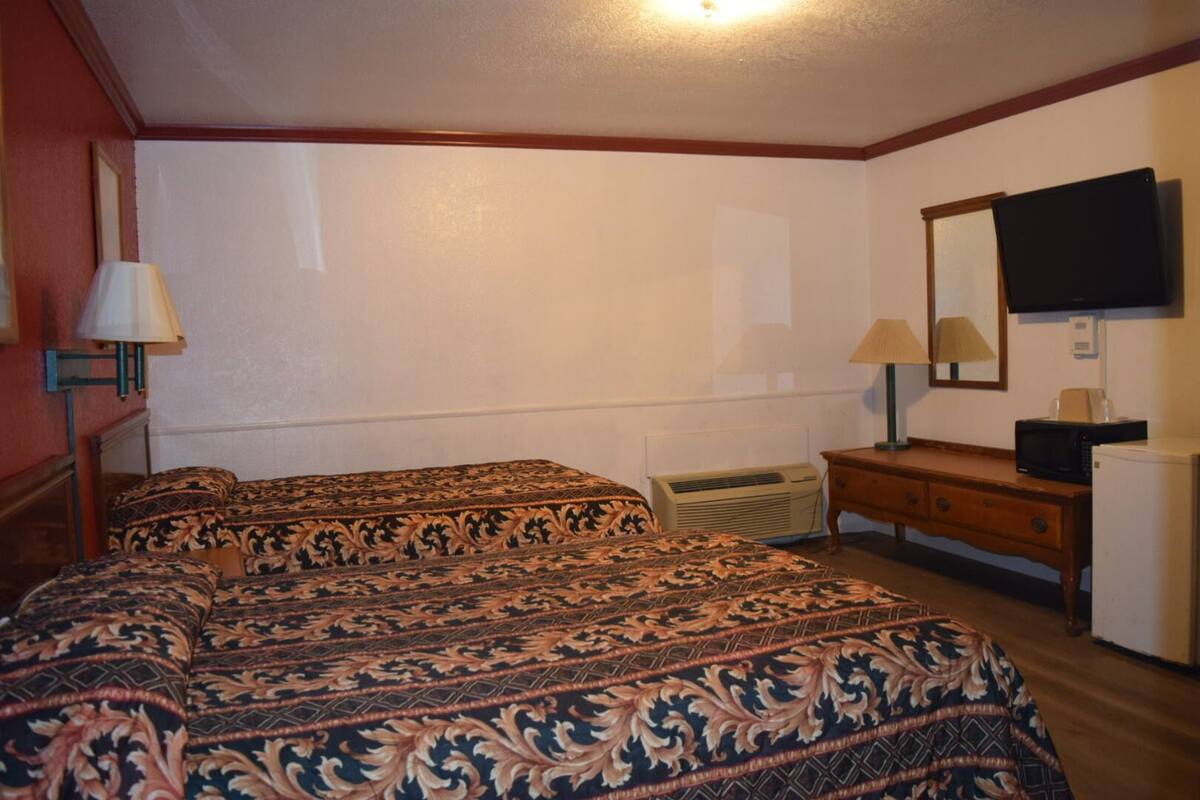 A hotel room with a large bed, two bedside lamps, a dresser, a mirror, a television, and an air conditioning unit.
