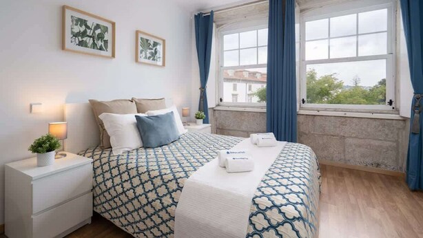 A hotel room with a bed, a nightstand, a lamp, and a window with curtains. - Peaceful & Sunny Building |One Terrace by HostWise (Porto)