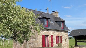 A stone building with red shutters and a sloped roof, surrounded by a wooden fence and a tree. - Au coin du châtaignier (Saint-Georges-de-Reintembault)