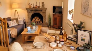 A cozy living room with a fireplace, a dining table set with plates, glasses, and a bottle, and a sofa with cushions. - Au coin du châtaignier (Saint-Georges-de-Reintembault)